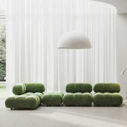 Ruangan minimalis bergaya kontemporer dengan cahaya alami dari jendela besar bertirai putih transparan, menampilkan sofa modular berumbai warna hijau zaitun, dan lampu gantung besar berbentuk kubah putih.